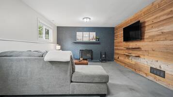A modern living room with a grey sectional sofa, a fireplace, and a flat-screen TV mounted on a wooden wall.