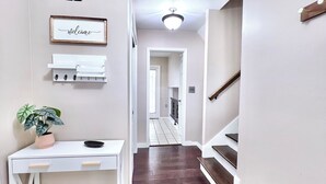 A hallway with a white console table, a welcome sign, a potted plant, and a wooden bench.