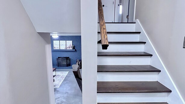 A staircase with dark wooden steps and white risers, leading to a room with a blue accent wall and a window.