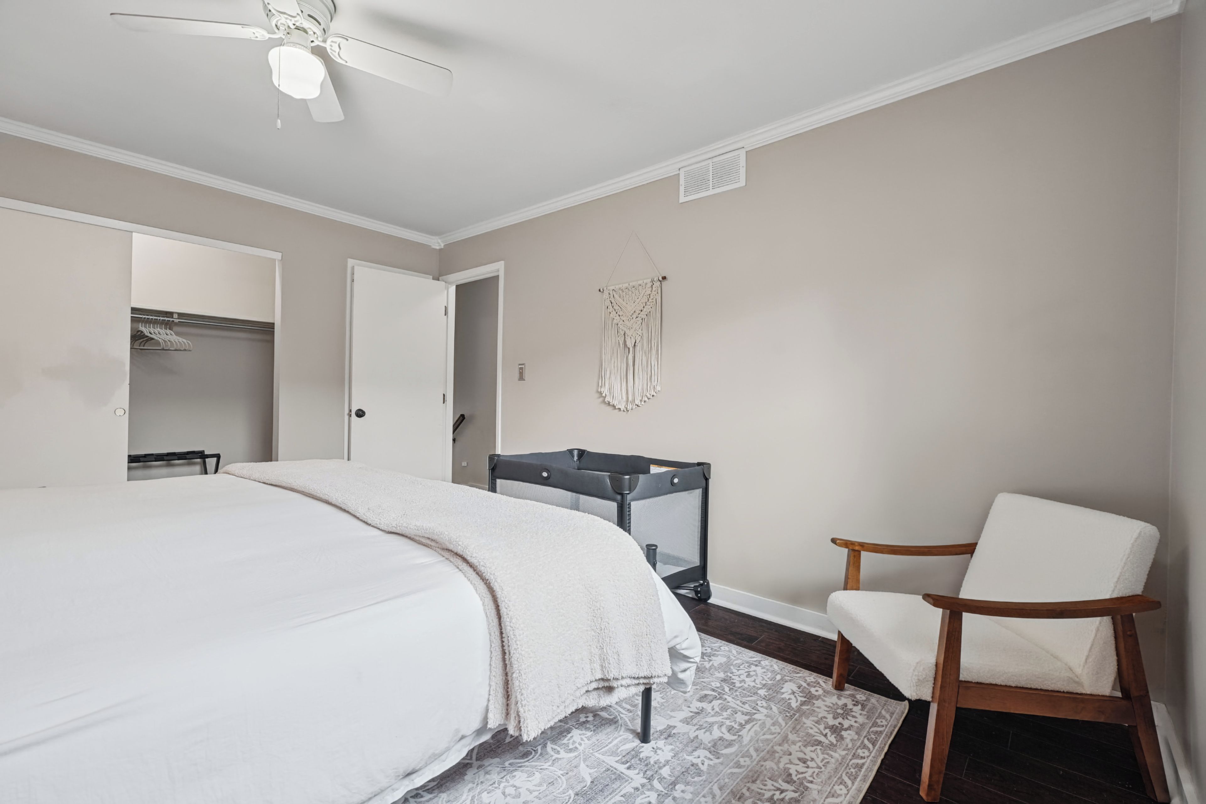 A bedroom with a bed, a chair, a crib, and a ceiling fan.