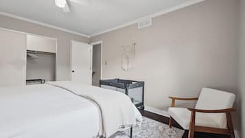 A bedroom with a bed, a chair, a crib, and a ceiling fan.