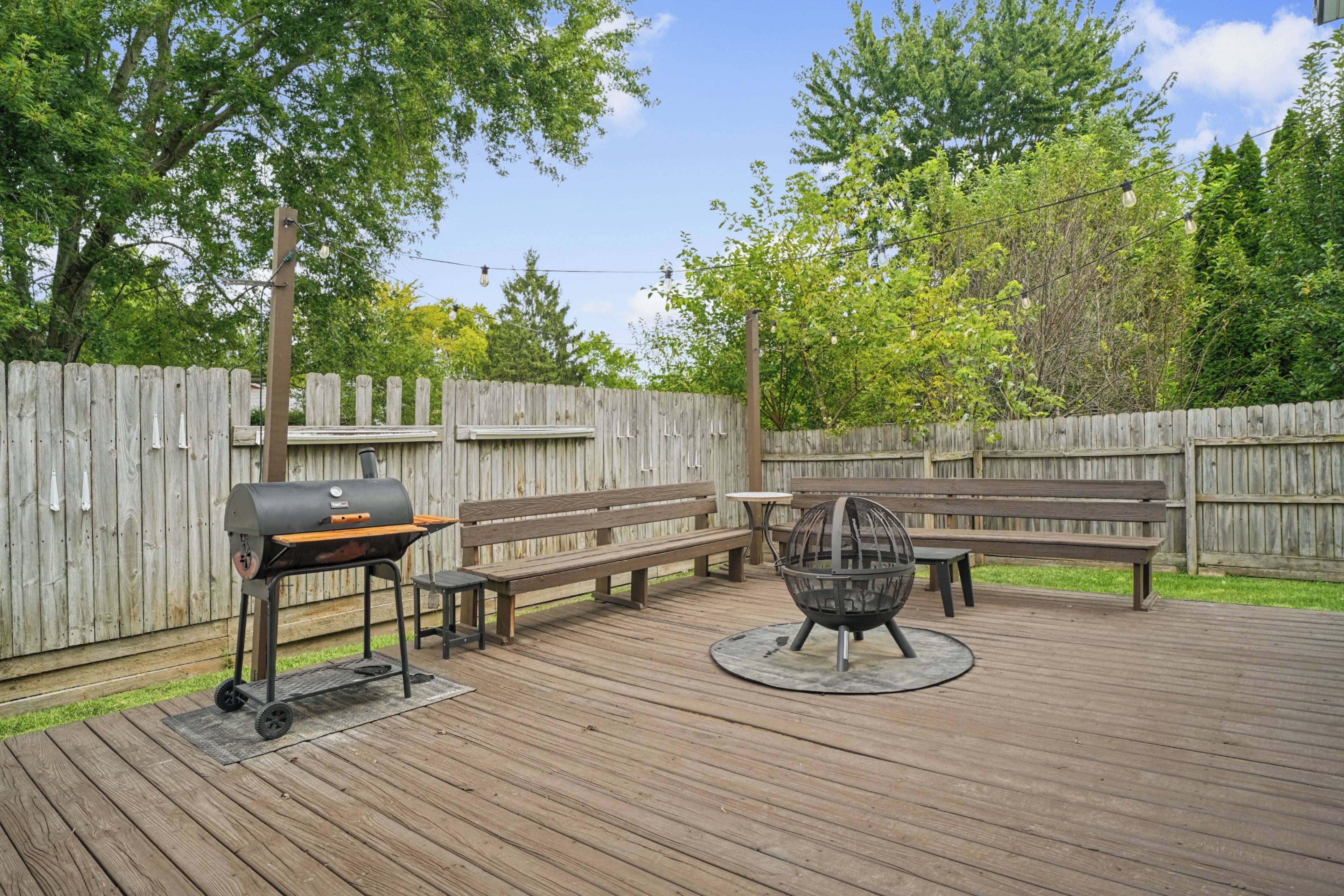 Une terrasse extérieure équipée d’un barbecue, d’un foyer rond et de bancs en bois.