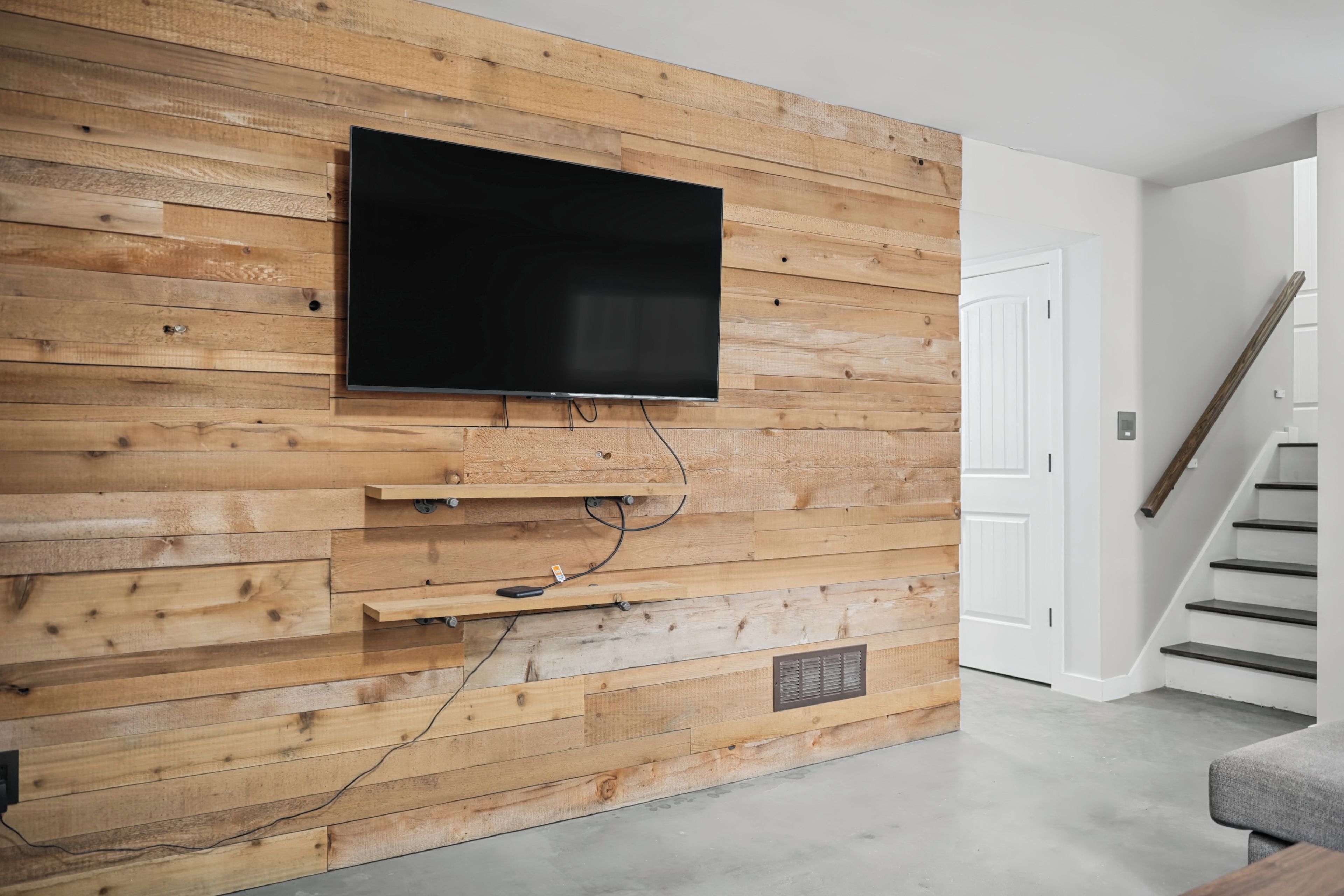 Un salon moderne avec un téléviseur à écran plat fixé à un mur en bois, un meuble de rangement intégré et un escalier menant à un autre niveau.