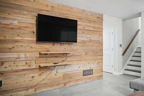 A modern living room with a flat-screen TV mounted on a wooden wall, a built-in entertainment unit, and a staircase leading to another level. - Spacious Family & Work-Friendly 3BD w/ Workspace, Fire Pit & Park Views Near Campus (Champaign)
