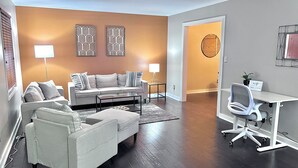 A modern living room with a sofa, armchair, and coffee table, a desk with a chair, and decorative wall art.