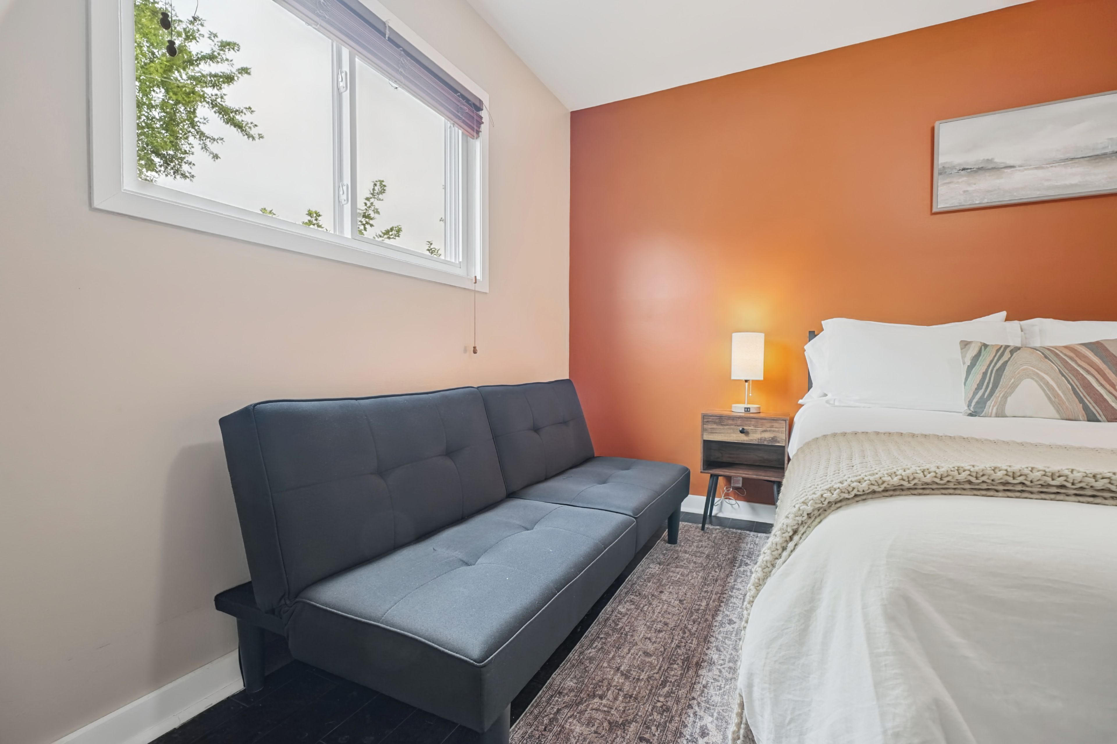 Une chambre d’hôtel avec un canapé, un lit, une table de chevet et une fenêtre donnant sur des arbres.