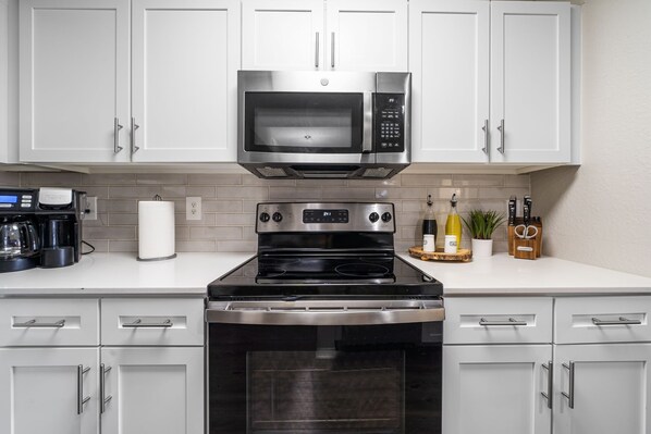 A modern kitchen with white cabinets, a stainless steel microwave, a stove, and a built-in oven.