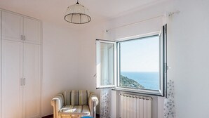 A bedroom with a bed, a chair, a wardrobe, a window with a view of the sea, and a radiator.