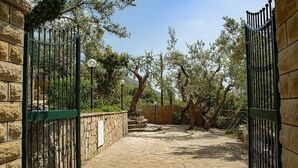 A stone-paved courtyard with a metal gate, stone walls, and trees.