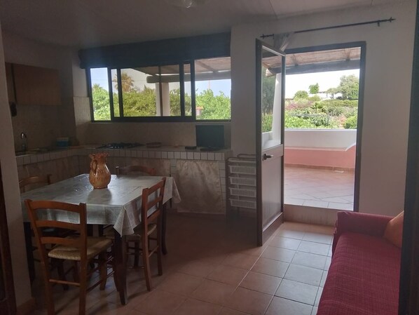 A dining area with a table and chairs, a kitchen area with a stove and sink, and a view of greenery through the windows.