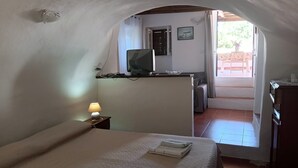 Une chambre à coucher avec un lit, une lampe de chevet, un bureau avec un ordinateur et une vue sur l’extérieur.