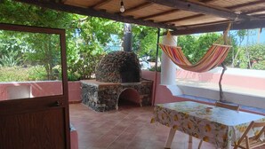 Une terrasse extérieure dotée d’un espace barbecue en pierre, d’un hamac et d’une table recouverte d’une nappe à motifs floraux.