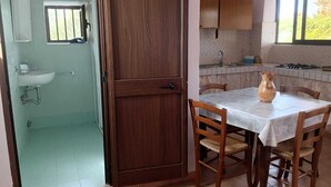 Une pièce avec une porte en bois, un lavabo, une fenêtre et une table avec des chaises.