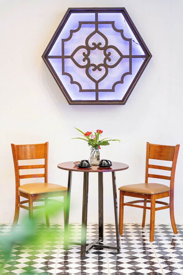 Un adorno mural hexagonal, una mesa redonda con dos sillas de madera y un jarrón con flores.