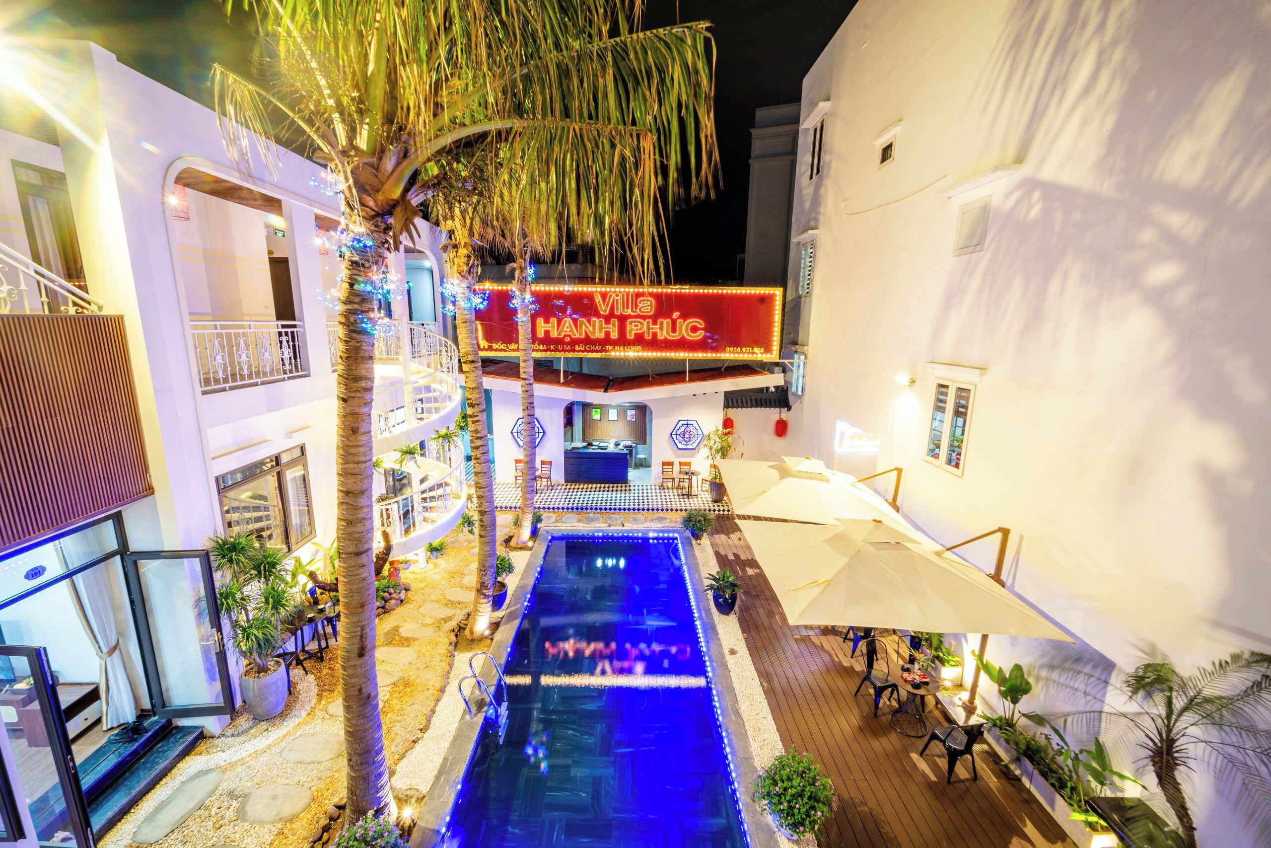 A pool area with a neon sign, palm trees, and outdoor seating.