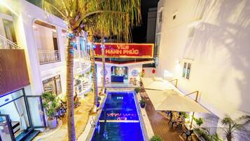 A pool area with a neon sign, palm trees, and outdoor seating.
