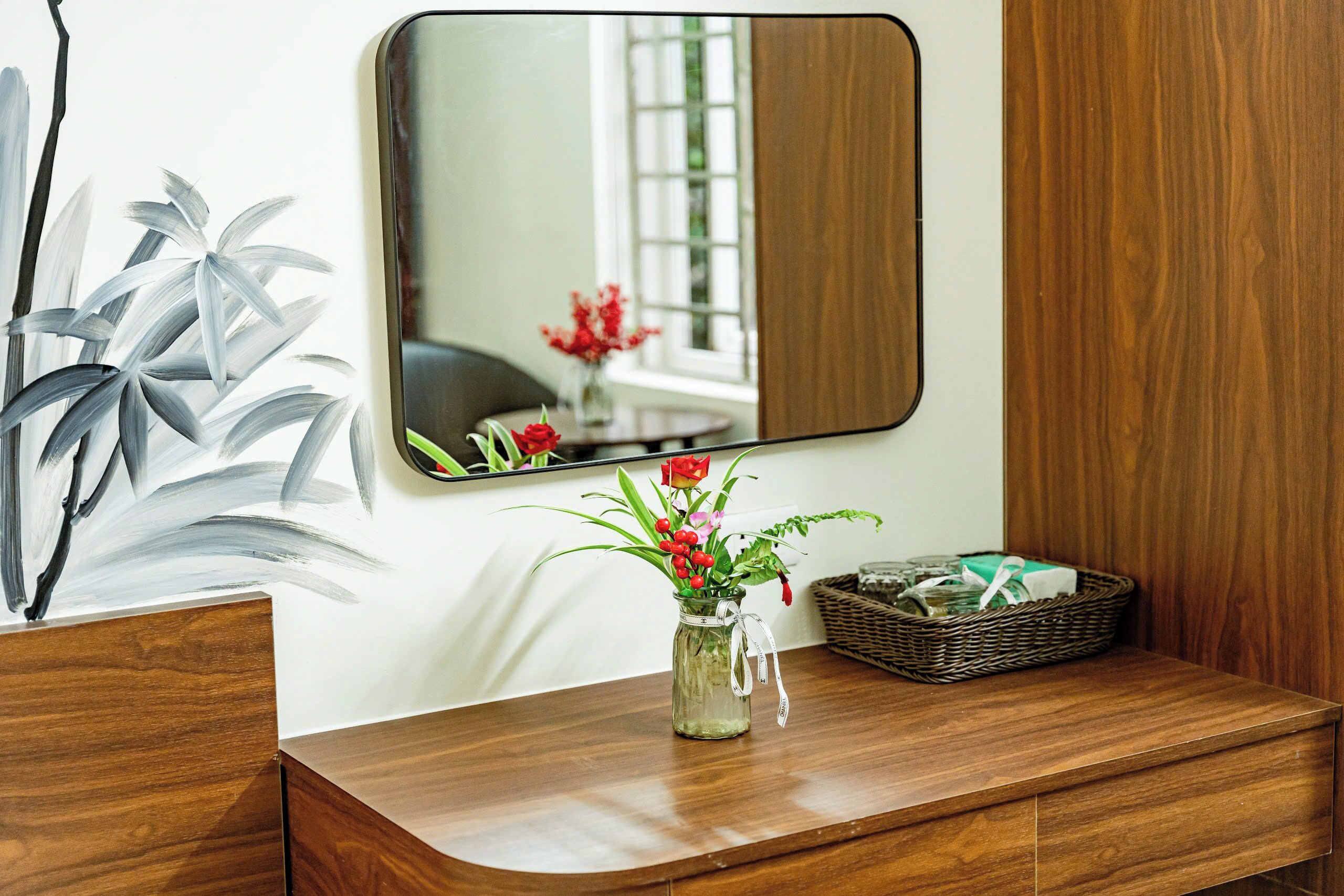 A wooden vanity with a mirror, a vase with flowers, and a wicker basket.