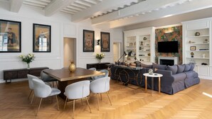 A spacious living room with a wooden herringbone floor, a dining area with a wooden table and modern chairs, a grey sofa, and a fireplace with decorative items.