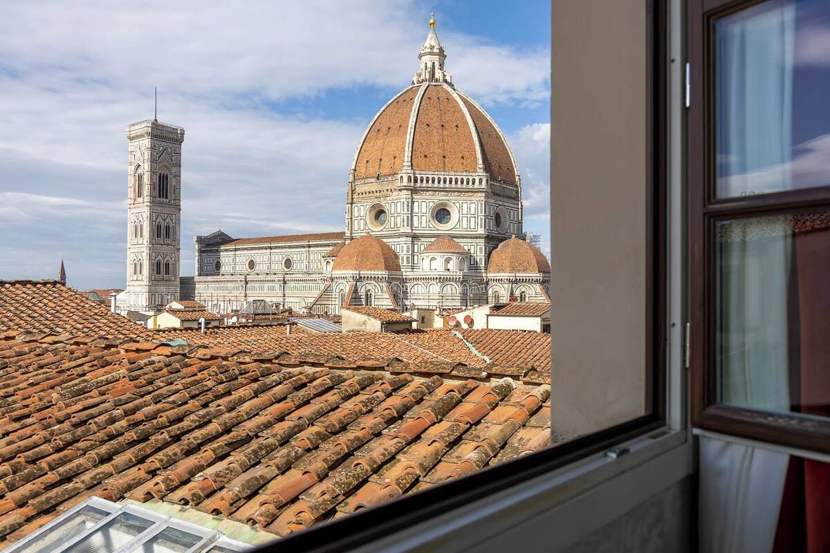 A view of the Florence Cathedral's dome and adjacent tower from a window overlooking a tiled roof.