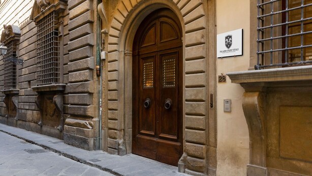 A historic building with a prominent arched entrance, a plaque indicating 'Palazzo Pazi Vitai', and a number '28' on the wall.