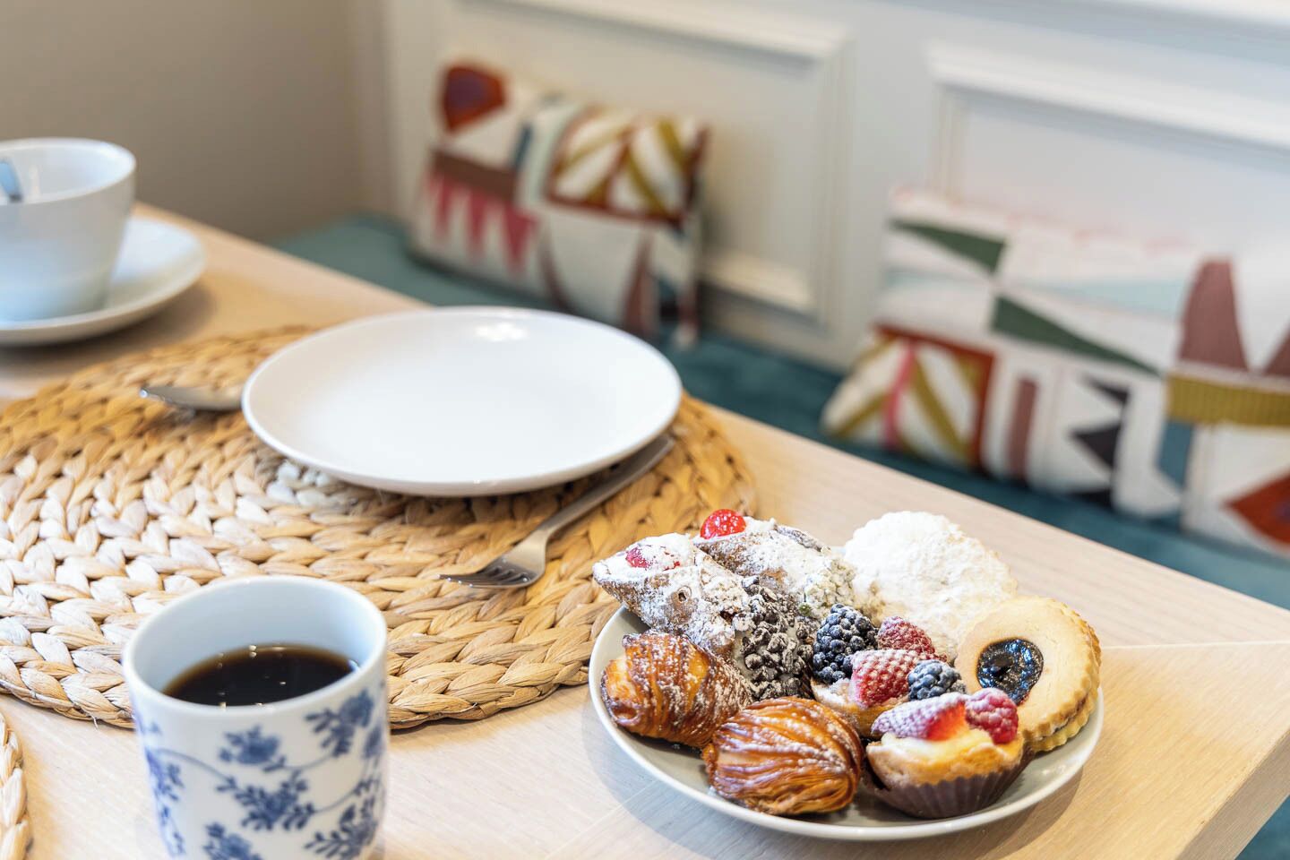 Une table dressée pour le petit-déjeuner avec des viennoiseries, une tasse de café et une assiette posée sur un set de table en fibres tressées.