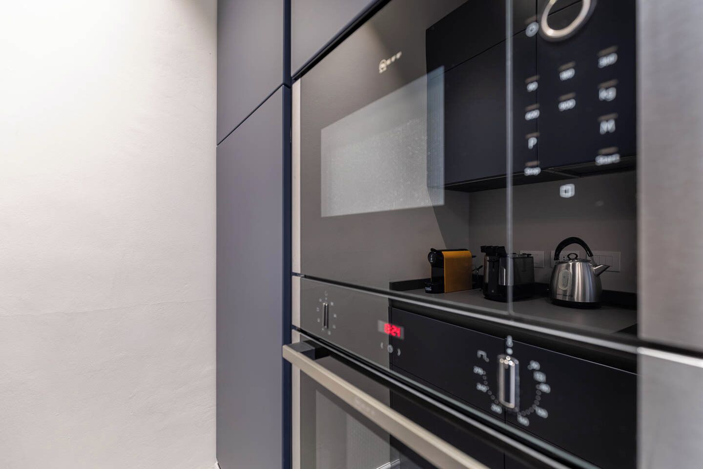 A kitchen with a built-in oven, a coffee maker, and a kettle on the countertop.