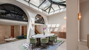 A spacious interior with a high ceiling, a central dining area with a round table and chairs, and a staircase leading to an upper level.