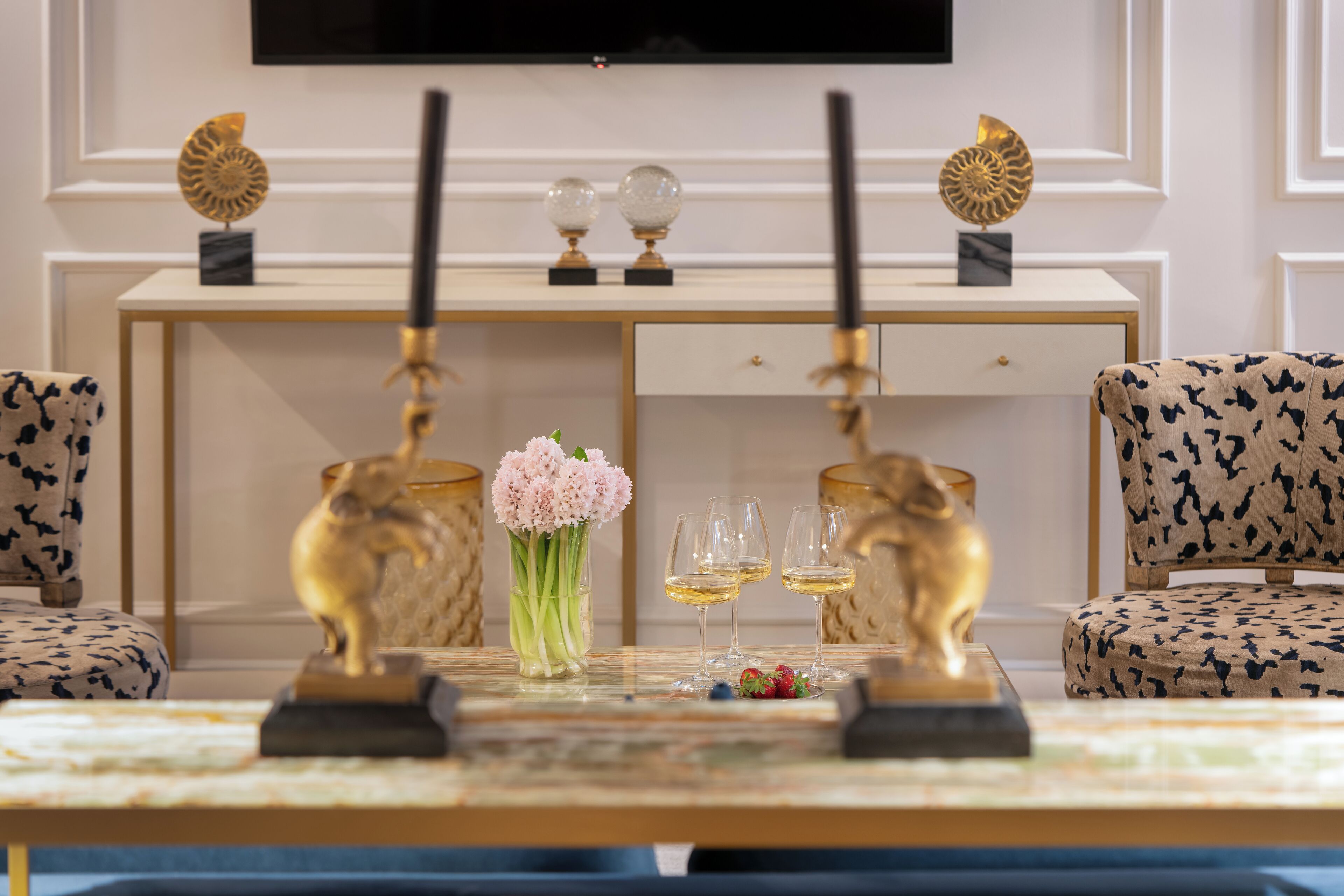 Ein luxuriöses Zimmer mit einem Marmortisch, zwei Sesseln, einer goldenen Statue, einem Blumenstrauß und zwei Weingläsern.