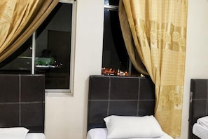 A hotel room with two beds, a window with curtains, and a view of a cityscape at night.