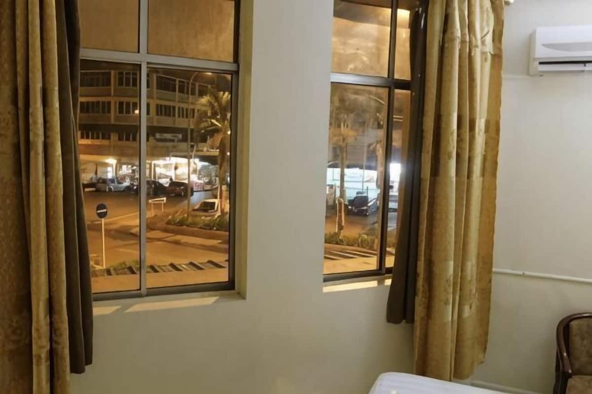 Una habitación con ventana que da a la calle, una cama y una silla.