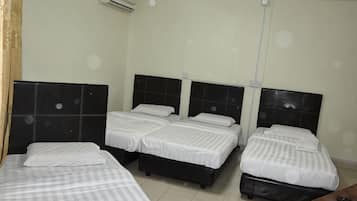 A hotel room with four beds, a wooden desk, and an air conditioning unit.