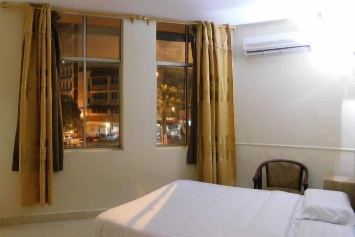 Una habitación de hotel con cama, una silla, una ventana con cortinas y un equipo de aire acondicionado.