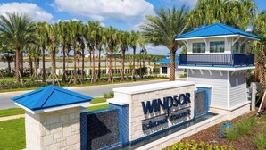 Une enseigne indiquant « Windsor Island Resort », avec un toit bleu et des murs blancs, entourée de palmiers et bordée par une étendue d’eau.