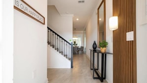 Ein Flur mit einer Treppe, einem Schild mit der Aufschrift 'IS OUR HAPPY PLACE', einem Konsolentisch mit einer Pflanze und einer Wandpaneelausstattung aus Holz.