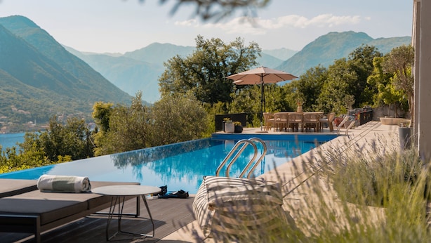 A pool with a view of mountains, surrounded by lounge chairs and a table.