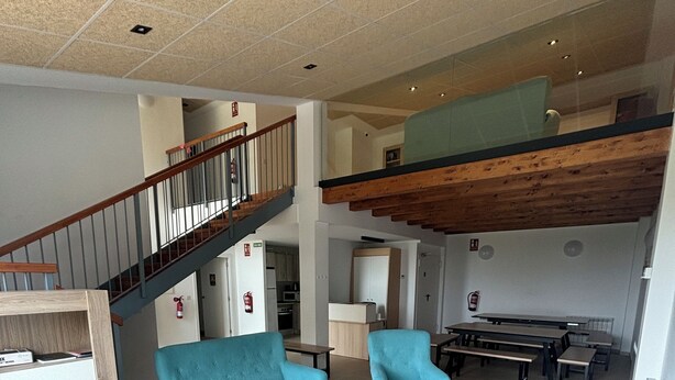 A spacious living area with a high ceiling, a wooden staircase, and a mezzanine level. - Albergue El Muro (Monforte de Moyuela)