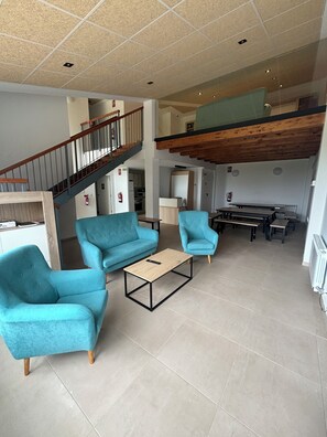 A spacious living area with a high ceiling, a wooden staircase, and a mezzanine level. - Albergue El Muro (Monforte de Moyuela)