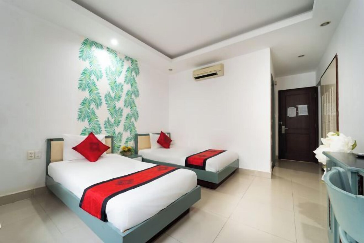 A hotel room with two beds, a desk, an air conditioning unit, and a door.