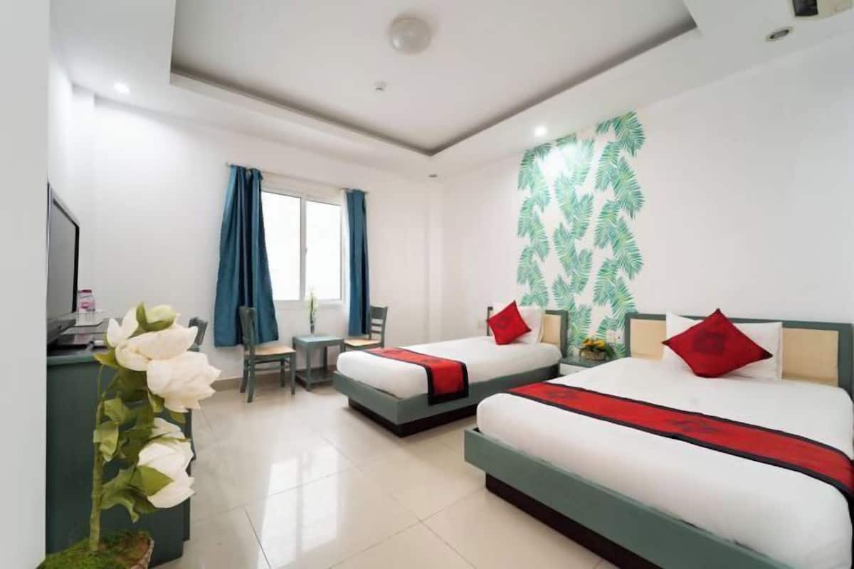 A hotel room with two beds, a desk, a chair, and a large window with curtains.