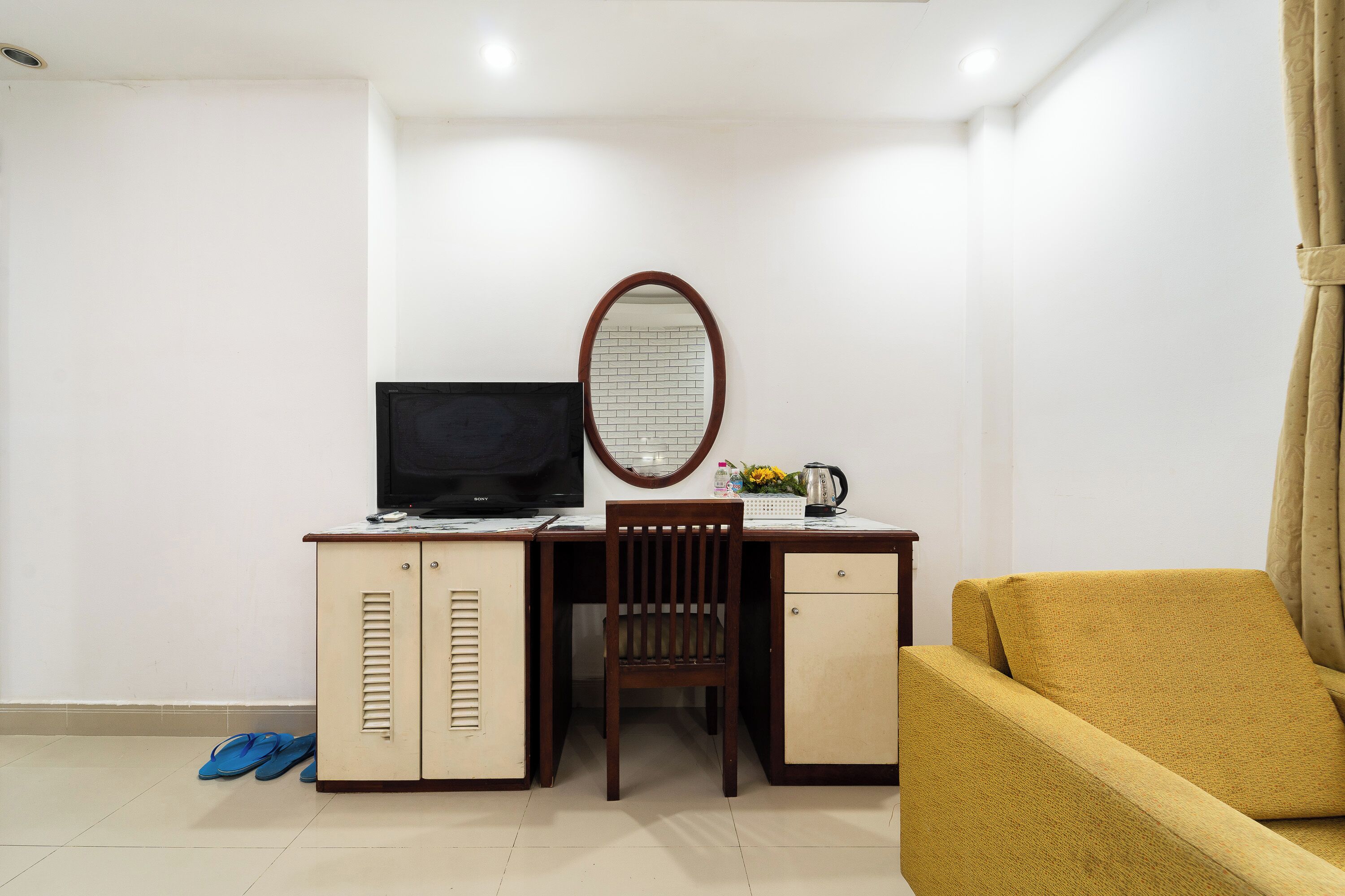 A compact hotel room with a desk, a chair, a sofa, a television, and a small cabinet.