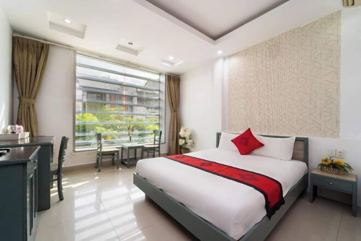 A modern hotel room with a bed, desk, and window with a view of greenery.