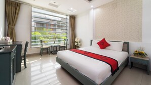 A hotel room with a bed, desk, chairs, and a view of greenery outside. - Collection O Cozy 5 Hotel - Near SECC (Ho Chi Minh City)
