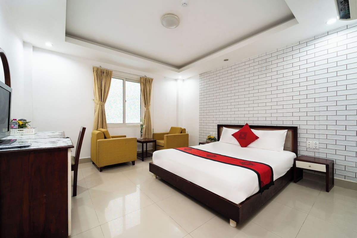 A hotel room with a bed, a desk, two chairs, a small table, and a window with curtains.
