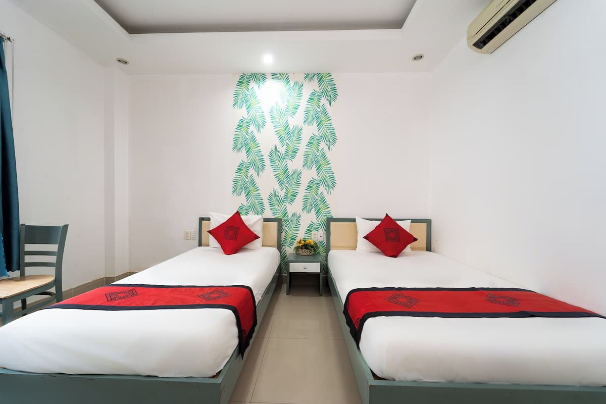 A room with two single beds, each with a red and black bedspread, white pillows, and a small table with a vase of flowers between them.