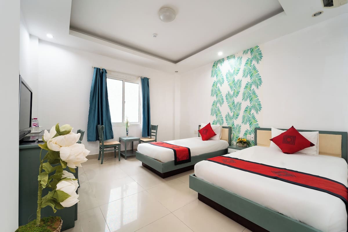 A hotel room with two beds, a desk, a chair, a window with curtains, and a decorative wall.