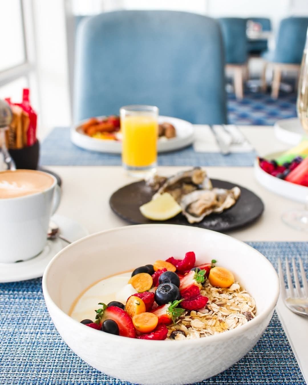 A breakfast setting with a bowl of cereal topped with fruits, a glass of orange juice, and a plate of eggs.