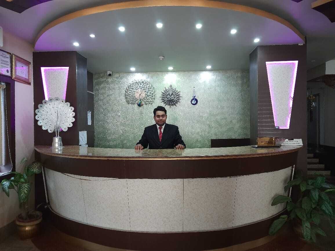 A reception desk with a man standing behind it, surrounded by decorative wall art and plants.
