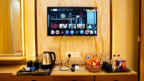 Un espace d’accueil d’hôtel avec un mur en marbre, un téléviseur à écran plat diffusant un festival de films, un coin café et un panier de collations.