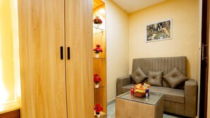 Une pièce avec une armoire en bois, un canapé beige, une table basse en verre sur laquelle sont posés des en-cas, et un tableau accroché au mur.