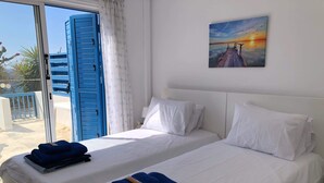 Ein Hotelzimmer mit zwei Betten, weißer Bettwäsche und einem Gemälde vom Sonnenuntergang über einem Steg.